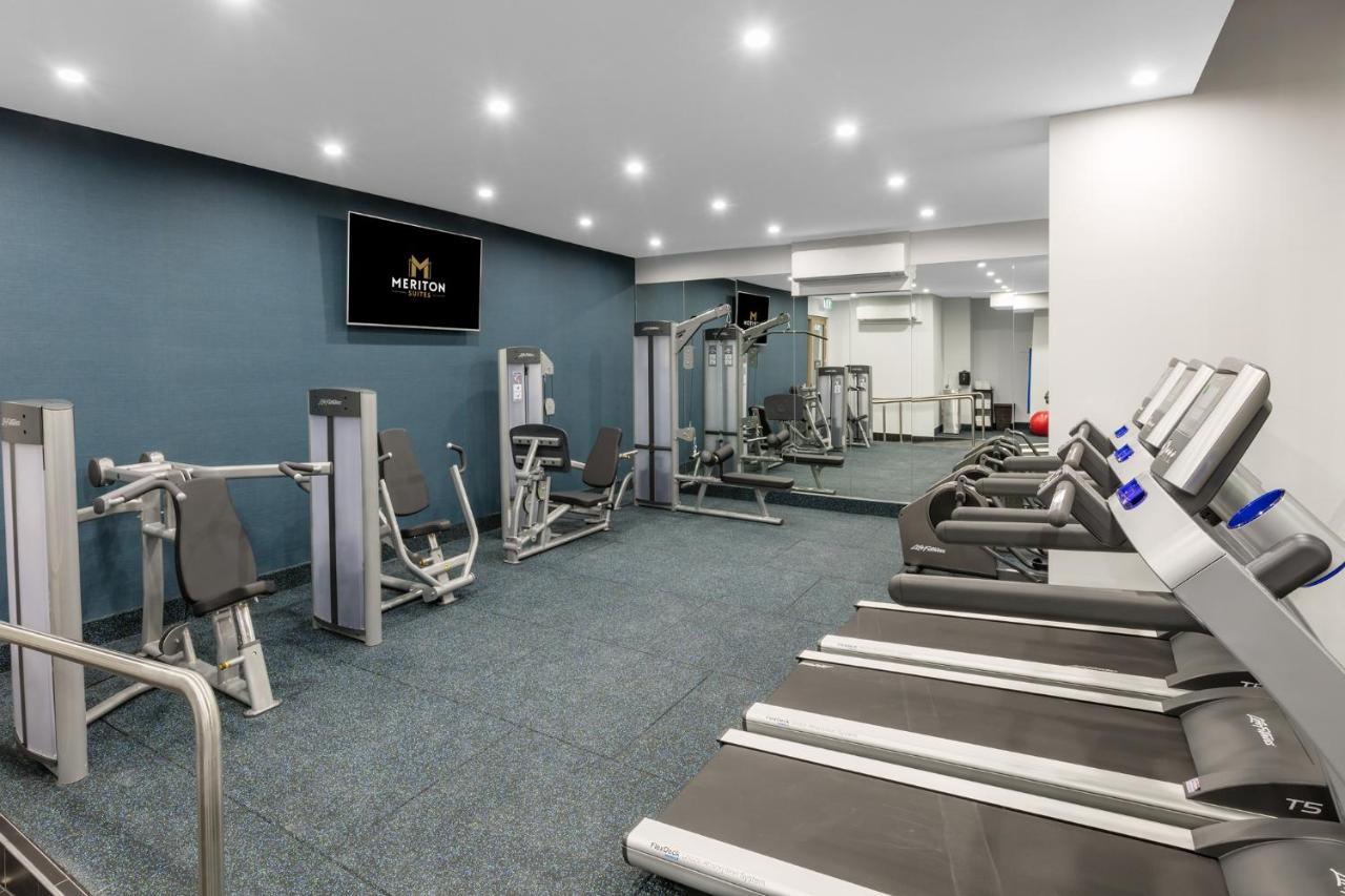 فندق أجنحة ميريتون سوسيكس ستريت سيدني المظهر الخارجي الصورة The photo shows a modern gym interior. The space features several pieces of exercise equipment, including weight machines and stationary bikes. The walls are painted a calming color, and the flooring is carpeted. There are also mirrors on the walls, 