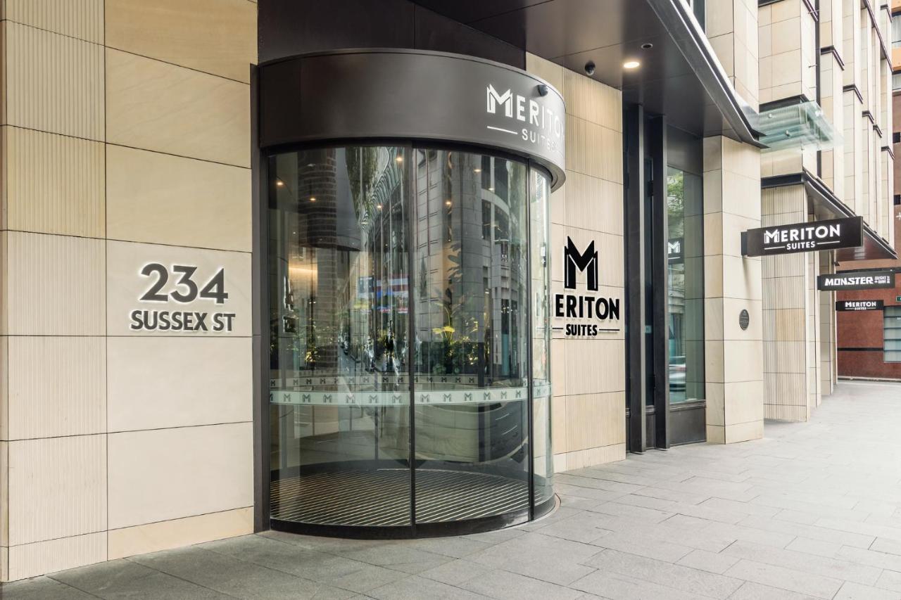فندق أجنحة ميريتون سوسيكس ستريت سيدني المظهر الخارجي الصورة The photo shows the entrance of a building located at 234 Sussex Street. It features a modern glass revolving door, alongside a sign indicating "Meriton Suites." The facade is characterized by a combination of stone and glass elements, reflecting a c