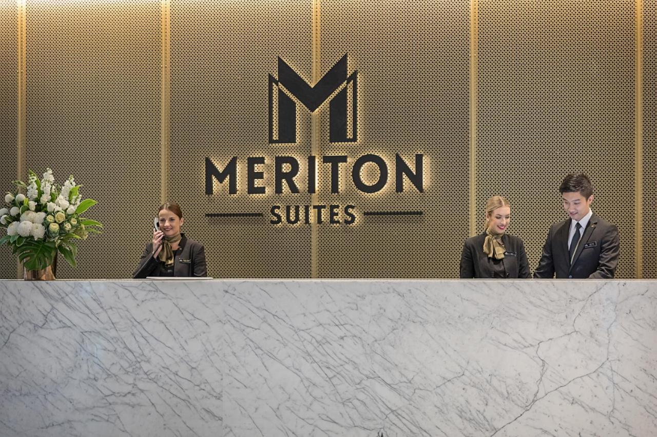 فندق أجنحة ميريتون سوسيكس ستريت سيدني المظهر الخارجي الصورة The photo depicts the reception area of a hotel called "Meriton Suites." In the background, there is a large, illuminated sign featuring the hotel’s logo. The reception desk is made of marble and is staffed by two individuals dressed in professional 