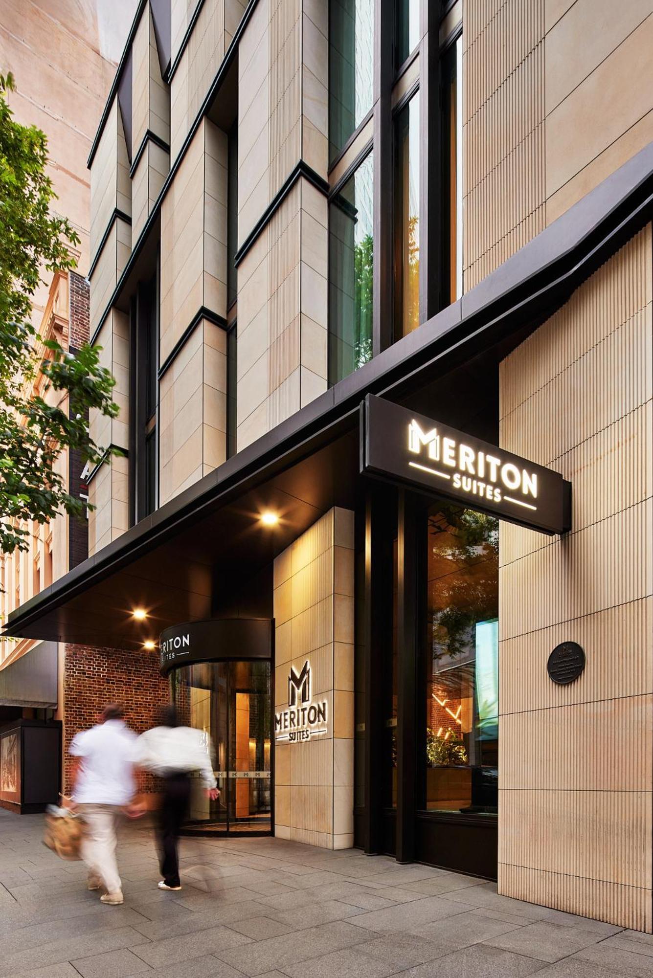 فندق أجنحة ميريتون سوسيكس ستريت سيدني المظهر الخارجي الصورة The photo shows the exterior of a building with the signage for "Meriton Suites." The entrance features a modern design, with sleek architectural elements and large windows. The entrance is highlighted by a prominent awning and illuminated signs, ind