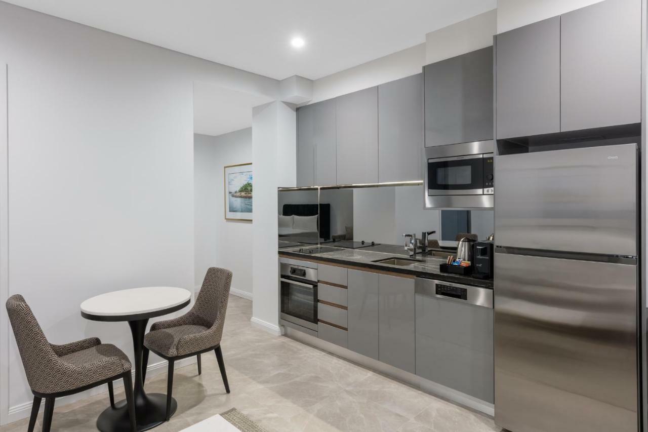 فندق أجنحة ميريتون سوسيكس ستريت سيدني المظهر الخارجي الصورة The photo shows a modern kitchen area that features a sleek design. The cabinetry and appliances are in shades of gray, giving it a contemporary look. There is a stainless steel refrigerator, microwave, and oven, along with a sink and cooking area. 
